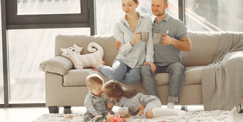 Cheerful family smiling while spending weekend together sitting parents sitting on comfortable sofa while children resting on carpet and playing